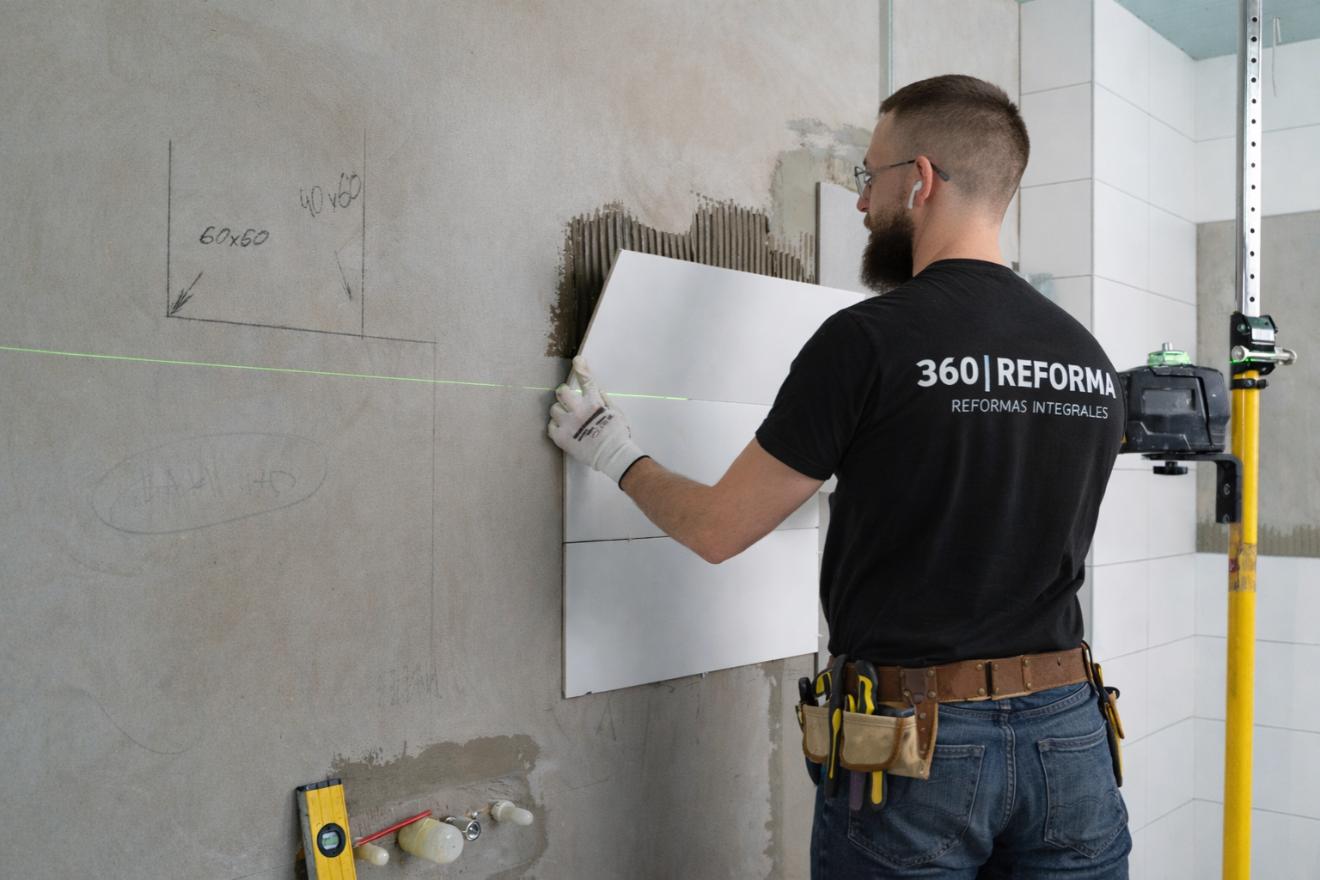Trabajador colocando azulejos en pared durante una reforma de baño en Lloret de Mar