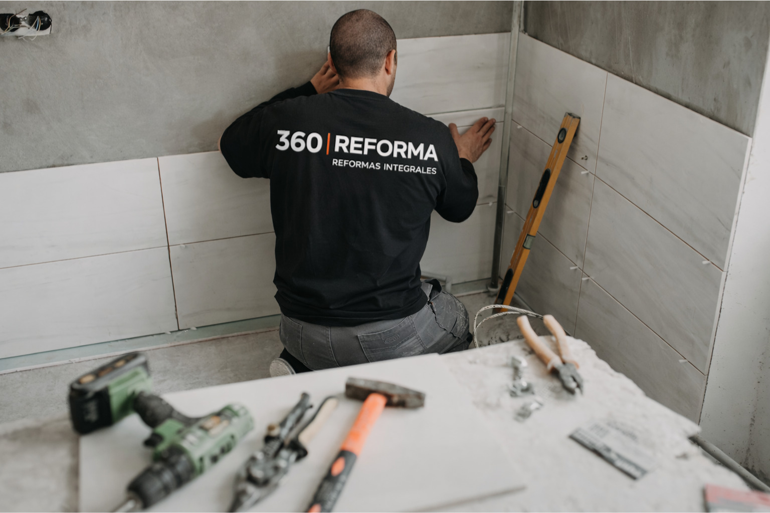trabajador realizando reforma de baño colocando azulejos en pared